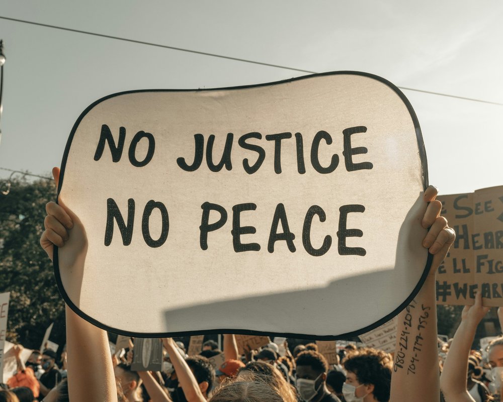A protester holds up a sign reading “No Justice, No Peace” above a crowd